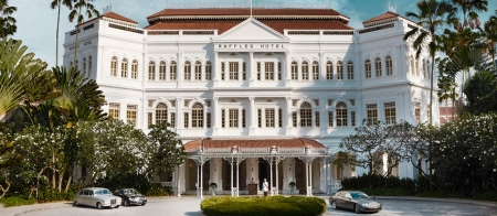 a large white building in front of a house with Raffles Hotel in the background