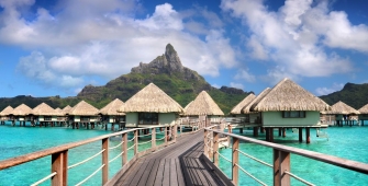a row of wooden benches sitting next to a body of water with Bora Bora in the background