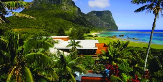 a group of palm trees next to a body of water with Lord Howe Island in the background