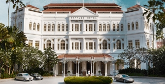 a large white building in front of a house with Raffles Hotel in the background