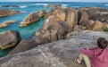 a group of people sitting on a rock near the ocean