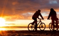 a man riding a bicycle with a sunset in the background