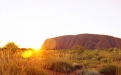 a sunset over a dry grass field with Uluru in the background