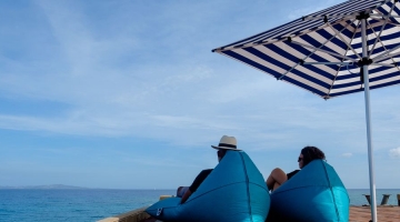 a man sitting at a beach umbrella next to a body of water