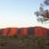 a large green field with trees in the background with Uluru in the background