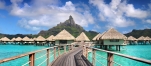 a row of wooden benches sitting next to a body of water with Bora Bora in the background