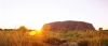 a sunset over a dry grass field with Uluru in the background
